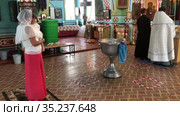 Godmother with goddaughter stand in the Orthodox church. The Priest with assistant are praying. Ceremony of sacrament of initiation into the Christian church (2021 год). Редакционное видео, видеограф Кекяляйнен Андрей / Фотобанк Лори