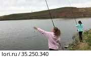 Two teenage girls catching fish with rods on lake shore. Recreational fishing in freshwater pond. Стоковое видео, видеограф Кекяляйнен Андрей / Фотобанк Лори