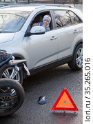 Warning triangle is in front of crash scene with car and motorcycle, scared woman a driver looking through the opened window, sitting inside a car. Стоковое фото, фотограф Кекяляйнен Андрей / Фотобанк Лори