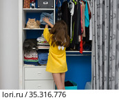 В открытом шкафу на полках с вещами сидят два кота, девочка кладет сложеную одежду на полку с котом. Стоковое фото, фотограф Иванов Алексей / Фотобанк Лори
