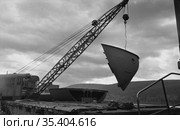 Речная гавань с подъёмным краном и фрагментом борта морского судна подвешенным к его стреле, река и лес на заднем плане, Осетрово, Чукотка, 1963 год. Стоковое фото, фотограф Варфоломей Тетерин / Фотобанк Лори