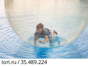 Little boy have fun inside big plastic balloon on the water of swimming pool on the summer resort. Kid inside big inflatable transparent ball running and having fun. Стоковое фото, фотограф Nataliia Zhekova / Фотобанк Лори