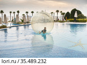 Little boy have fun inside big plastic balloon on the water of swimming pool on the summer resort. Kid inside big inflatable transparent ball running and having fun. Стоковое фото, фотограф Nataliia Zhekova / Фотобанк Лори