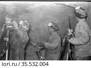 Несколько молодых людей находятся в небольшой шахте, они занимаются бурением каминных плит для добычи слюды, большие шахтёрские буры в руках у мужчин, Эмельджак, Якутия, 1961. Редакционное фото, фотограф Варфоломей Тетерин / Фотобанк Лори