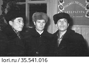 Трое мужчин среднего возраста позируют в здании клуба, плакат с портретами писателей и надписью художественной литературы позади них, Поселок Эмельджак, Якутия, 1961 год. Редакционное фото, фотограф Варфоломей Тетерин / Фотобанк Лори