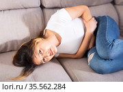 Mexican female at sofa holding hands on the illness stomache. Стоковое фото, фотограф Яков Филимонов / Фотобанк Лори
