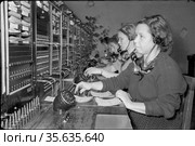 Несколько женщин разных возрастов работают телефонистками на междугородней телефонной станции, девушки сидят за столом с большим количеством радио оборудования и соединяют звонящих друг с другом, Якутия, октябрь 1959. Редакционное фото, фотограф Варфоломей Тетерин / Фотобанк Лори