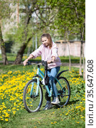 Portrait of teenager Caucasian girl standing with bicycle in spring park with yellow flowers. Стоковое фото, фотограф Кекяляйнен Андрей / Фотобанк Лори