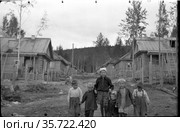 Дети гуляют по ухабистая деревенской улице, несколько мальчиков и девочек идут по грунтовой дороге, деревянные дома и высокие ели на заднем плане, город Керенск, август 1956. Редакционное фото, фотограф Варфоломей Тетерин / Фотобанк Лори