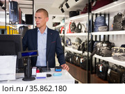 Concentrated man standing at a computer in a store, specifying the price of the desired goods. Стоковое фото, фотограф Яков Филимонов / Фотобанк Лори
