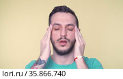 Young man suffering from severe headache, pressing fingers to temples, closing eyes in order to relieve pain. Стоковое видео, видеограф Mihail Mihaylov / Фотобанк Лори