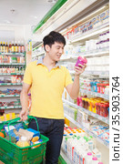 Smiling Young Man Looking At Food in Supermarket. Стоковое фото, агентство Ingram Publishing / Фотобанк Лори
