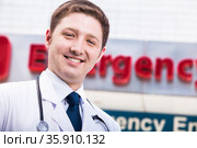 Portrait of young smiling doctor outside of the hospital, emergency room sign in the background. Стоковое фото, агентство Ingram Publishing / Фотобанк Лори