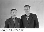 Портрет двух мужчин стоящих в помещении рядом с белой стеной, один из них улыбается другой позирует с серьёзным выражением лица, Якутия, ноябрь 1963, база Холбос. Стоковое фото, фотограф Варфоломей Тетерин / Фотобанк Лори