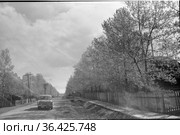 Автомобиль едет по центральной улице города Алдан, асфальтированная дорога с деревянными линиями электропередач и оградой у обочины, Якутия, июнь 1965. Стоковое фото, фотограф Варфоломей Тетерин / Фотобанк Лори