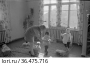 Маленькие девочки в детском саду при полярный научные станции, женщина и ребёнок стоят в помещении рядом с множеством игрушек, окна на заднем плане, село Уэлен, Чукотка, 1970. Редакционное фото, фотограф Варфоломей Тетерин / Фотобанк Лори