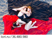 Две прекрасные девушки в черных купальниках лежат свернувшись калачиком на красной и черной ткани на песочном пляже. Вид сверху. Стоковое фото, фотограф Евгений Ткачёв / Фотобанк Лори