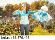 Happy girl holding package for garbage. Young woman volunteer, participates in an environmental campaign and removes plastic garbage in the park. Concept ESG and SDGs. Стоковое фото, фотограф Сергей Тимофеев / Фотобанк Лори