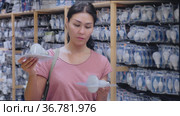 Adult Asian woman choosing bulbs in housewares store. She's holding two packs in hands and comparing them. Стоковое видео, видеограф Яков Филимонов / Фотобанк Лори