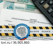 Договор аренды недвижимого имущества, оградительная лента с эмблемой Федеральной налоговой службы и надписью "налоги", калькулятор и деньги (2021 год). Редакционное фото, фотограф Цибаев Алексей / Фотобанк Лори