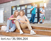 Girl prompts solution to problem to young man sitting on stone staircase in front of school. Стоковое фото, фотограф Яков Филимонов / Фотобанк Лори