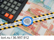 Оградительная лента с эмблемой федеральной налоговой службы и надписью "налоги", калькулятор и российские деньги (2021 год). Редакционное фото, фотограф Цибаев Алексей / Фотобанк Лори