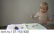 A little girl in pajamas is walking near a table with water markers for children. There is a reusable tablecloth on the table for drawing. Стоковое видео, видеограф Наталья Гармашева / Фотобанк Лори