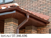 Corner of house with new brown metal tile roof and rain gutter. Metallic Guttering System, Guttering and Drainage Pipe Exterior. Стоковое фото, фотограф Данила Большаков / Фотобанк Лори