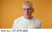 Senior man in glasses have doubts looking suspicious on yellow background. Стоковое видео, видеограф Сергей Толмачёв / Фотобанк Лори