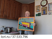 Наивный художник Владимир Аносов со своей работой на кухне (2022 год). Редакционное фото, фотограф Дмитрий Неумоин / Фотобанк Лори