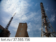 Plant chimney (smoking stack) and pipelines of phosphoric fertilizers plant on blue sky with sun background. Chemical industry. Стоковое фото, фотограф Alexey Rezvykh / Фотобанк Лори