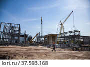 Old phosphate fertilizer plant in modernization. Construction of new industrial buildings. Mobile cranes, building steel structure, one worker. On blue sky background. Стоковое фото, фотограф Alexey Rezvykh / Фотобанк Лори