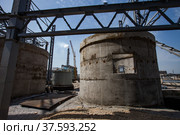 Phosphate fertilizers plant. Grey round concrete construction and girder crane and plant chimney on blue sky background. Assembling a metal structure of new industrial building. Стоковое фото, фотограф Alexey Rezvykh / Фотобанк Лори