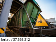 Handmade yellow "Train" road sign. Focus on foreground. Green hopper car on rails blurred on background. Loading and filling terminal of fertilizers plant. Стоковое фото, фотограф Alexey Rezvykh / Фотобанк Лори