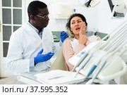 Woman patient who came to an appointment with a male dentist is sitting in a dental chair in clinic office, showing which side of her tooth aches. Стоковое фото, фотограф Яков Филимонов / Фотобанк Лори