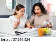 Two women with financial documents near laptop sitting at table at home. Стоковое фото, фотограф Яков Филимонов / Фотобанк Лори