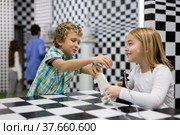 Boy adn girl solving puzzle together in room stylized like chessboard. Стоковое фото, фотограф Яков Филимонов / Фотобанк Лори