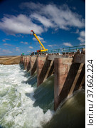 Kok-aral, Kazakhstan - May 03, 2012: Small Aral Sea Kok-aral dam. Water discharge in flood. Open shutters. Yellow mobile crane and workers on dam. Стоковое фото, фотограф Alexey Rezvykh / Фотобанк Лори