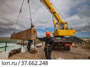 Kok-aral, Kazakhstan - May 03, 2012: Small Aral Sea Kok-aral dam. Lifting water shutter weighting agent (girder). Yellow mobile crane. Adult Asian worker in orange hardhat. Редакционное фото, фотограф Alexey Rezvykh / Фотобанк Лори