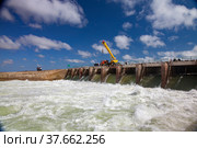 Small Aral Sea Kok-aral dam.Water discharge in flood. Open gates. Yellow mobile crane and workers on dam. Стоковое фото, фотограф Alexey Rezvykh / Фотобанк Лори