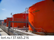 Orange metal storage tanks with acid and its formula on sulfuric (sulphuric) acid plant warehouse. Clear blue sky. Стоковое фото, фотограф Alexey Rezvykh / Фотобанк Лори
