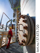 Aktobe region/Kazakhstan - May 04 2012: Oil refinery plant. Technician in red work wear and yellow helmet on refining column. CNPC company. Редакционное фото, фотограф Alexey Rezvykh / Фотобанк Лори
