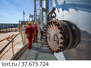 Aktobe region/Kazakhstan - May 04 2012: Oil refinery plant. Two maintenance workers in red work wear and yellow helmets on refining column. On pipelines and blue sky background. CNPC company. Редакционное фото, фотограф Alexey Rezvykh / Фотобанк Лори