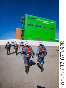 Khromtau, Aktobe region, Kazakhstan - May 06 2012: Group of miners in white hardhats go to the green concentration plant (processing plant) building. Mechel company. Редакционное фото, фотограф Alexey Rezvykh / Фотобанк Лори