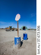 Khromtau, Aktobe region, Kazakhstan - May 06 2012: Hand-made and fade road sign STOP on plastic barrel with concrete. Gold mine portal and Caterpillar bulldozer (tractor) on background. Редакционное фото, фотограф Alexey Rezvykh / Фотобанк Лори