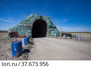 Khromtau, Aktobe region, Kazakhstan - May 06 2012: Gold ore mine portal. Title: Quarry and Mechel company logo. Blue plastic barrel with concrete. Blue sky and desert road. Редакционное фото, фотограф Alexey Rezvykh / Фотобанк Лори