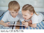 Дети и гаджеты. Мальчик с девочкой лежат на кровати и смотрят в планшет. Стоковое фото, фотограф Владимир Ходатаев / Фотобанк Лори