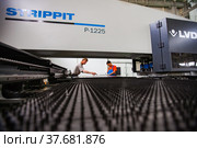 Aktau, Kazakhstan - May 05, 2012: CNC laser cutting machine LVD and two workers (in focus). Production of special electric equipment. RIG Ltd. Редакционное фото, фотограф Alexey Rezvykh / Фотобанк Лори