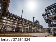 Uralsk region, Kazakhstan - May 24 2012: Oil deposit Zhaikmunai. Oil refinery and gas processing plant. Distillation tower (refinery column) and pipelines on blue sky with sun background. Стоковое фото, фотограф Alexey Rezvykh / Фотобанк Лори