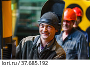Ekibastuz, Pavlodar region, Kazakhstan - May 28, 2012: Rail car-building plant. Young welder in protective mask smiling and posing. Another persons blurred. Редакционное фото, фотограф Alexey Rezvykh / Фотобанк Лори